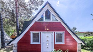 Una casa roja con puerta y ventanas blancas, un porche pequeño y cimientos de piedra.