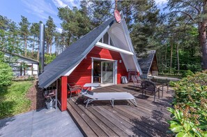 A red cabin with a sloped roof, a deck with a lounge chair and table, and a satellite dish.