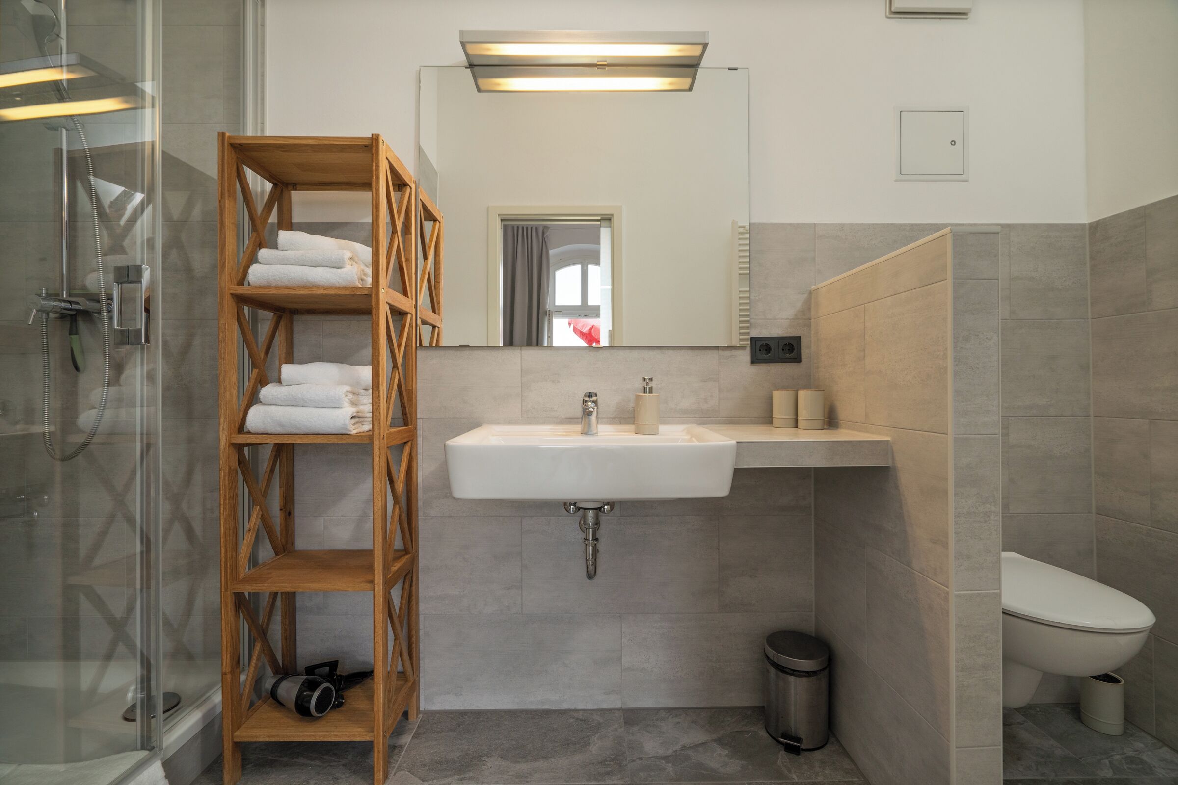 Ein modernes Badezimmer mit Duschkabine aus Glas, einem Holzhandtuchhalter, einem Waschbecken mit Spiegel und einer Toilette.