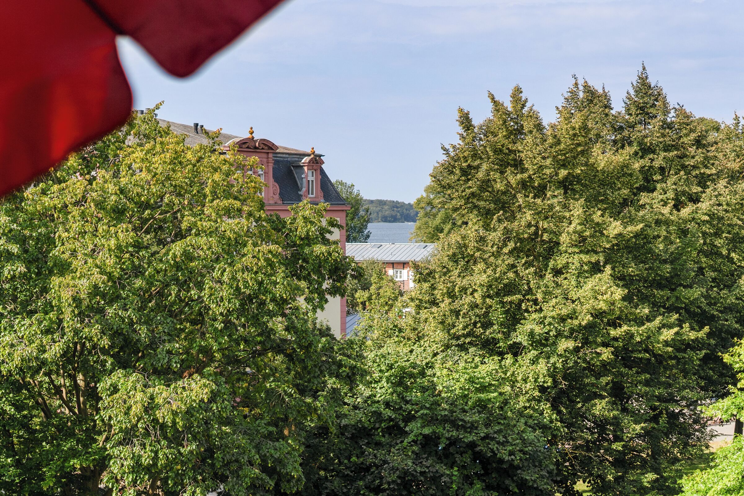 Ein Gebäude mit rotem Dach und einem Turm, umgeben von dichtem Grün.