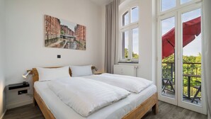 Una habitación de hotel con una cama grande, una mesita de noche, un ventanal con vistas y un paraguas rojo afuera.