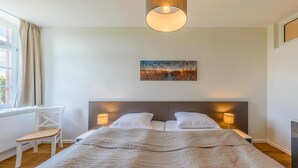 A neatly made bed with a quilted blanket, a bedside lamp, and a painting on the wall.