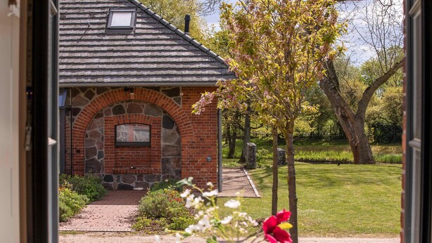 A brick building with a stone archway entrance, surrounded by a well-maintained garden and trees.