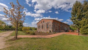 A stone building with a red roof, a paved pathway, and a grassy area with a bench.
