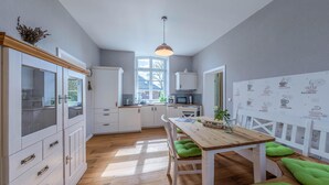 A modern kitchen with white cabinets, a wooden table, and green cushioned seating.