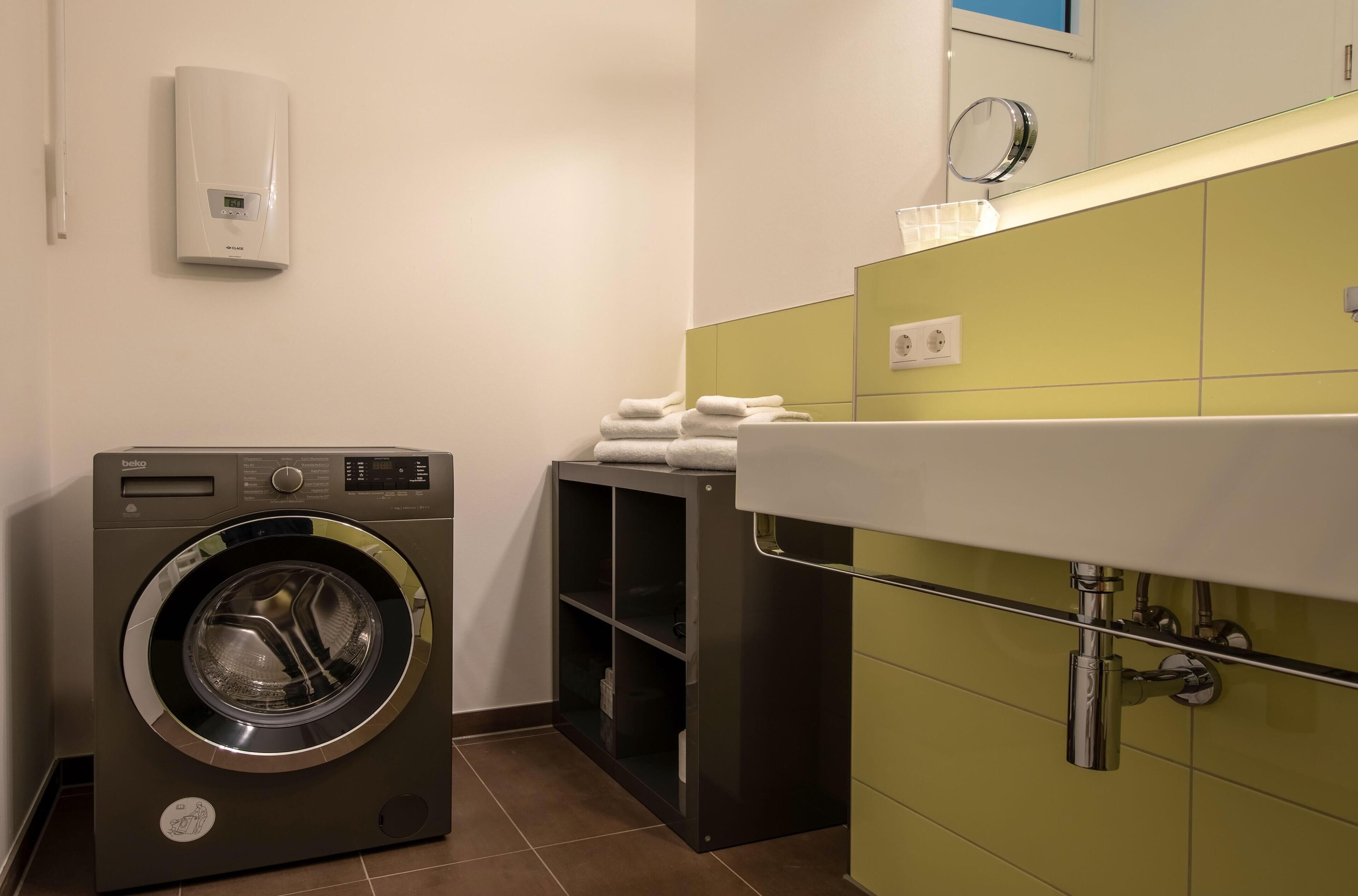 Un espace buanderie compact comprenant un lave-linge à chargement frontal, un étendoir et un évier avec un miroir au-dessus.