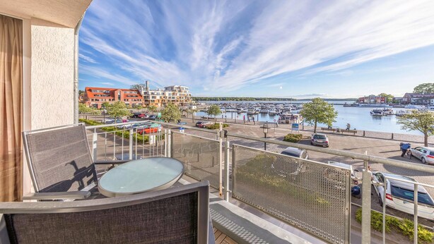 A balcony with a table and chairs overlooking a marina with boats and a parking area.