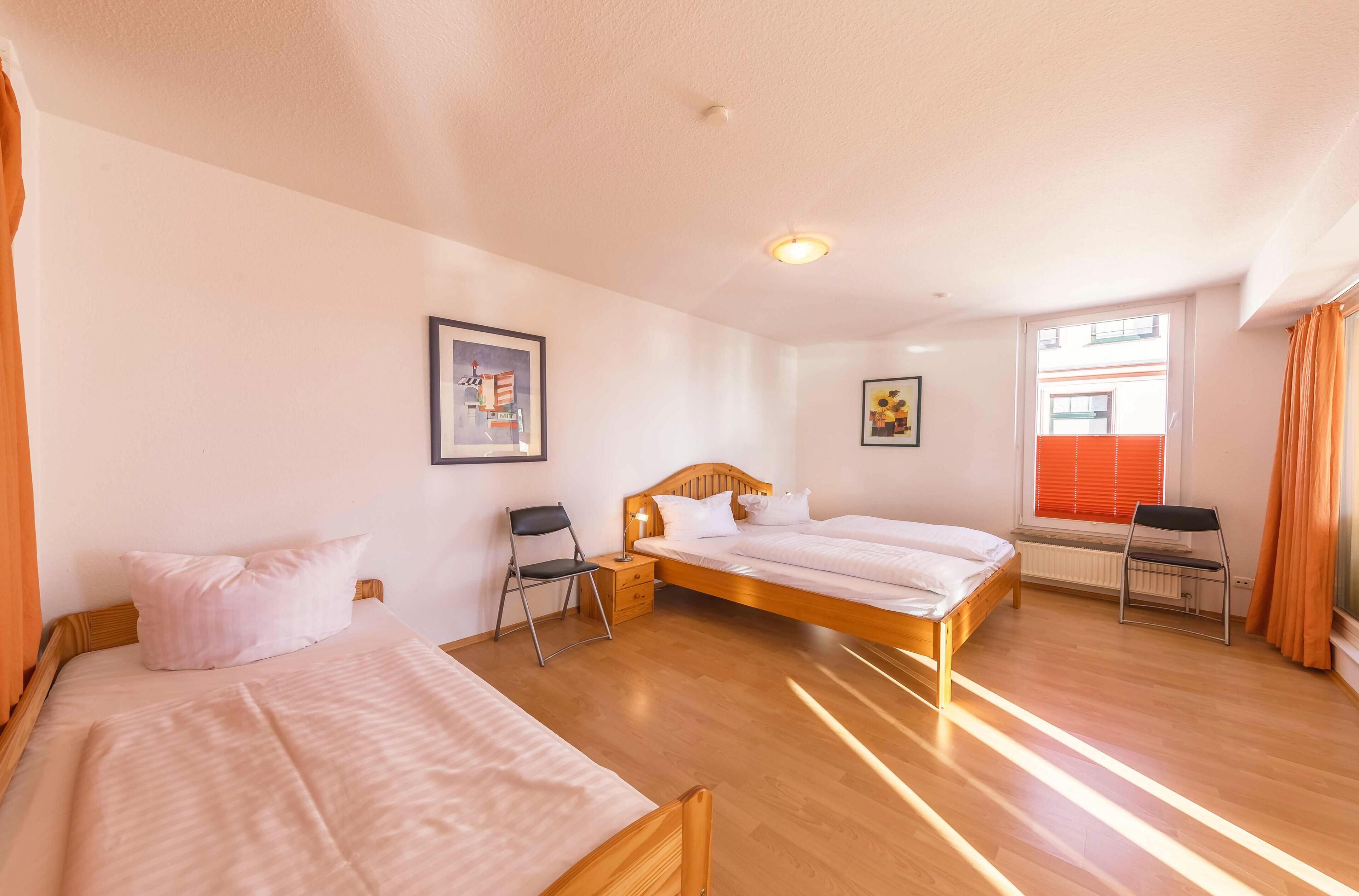 Ein Hotelzimmer mit zwei Einzelbetten, Holzboden, einem Fenster mit orangefarbenen Jalousien und einem Heizkörper.