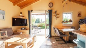 Un salón acogedor con techo de madera, televisor, sofá, mesa de comedor con sillas y vistas al exterior.