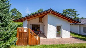 Een gelijkvloers huis met een overdekt terras, een houten poort en een pad van stenen tegels dat naar de ingang leidt.