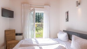 Een slaapkamer met een bed, een stoel, een televisie en een raam met gordijnen.
