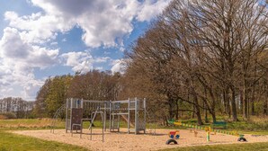 Une aire de jeux avec une structure en métal, du sable et des arbres en arrière-plan.
