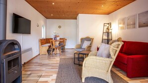 Un salon chaleureux avec une cheminée, un canapé rouge, des fauteuils en osier et un coin repas avec des meubles en bois.
