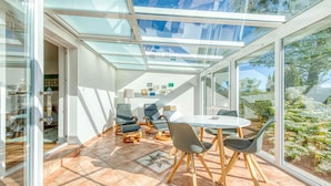 Eine sonnendurchflutete Terrasse mit Glasdach, Sitzgelegenheiten im Freien und Blick ins Grüne.