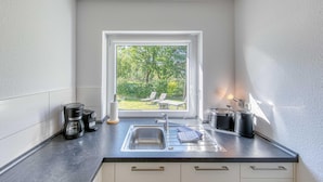 Eine Küche mit Fensterblick auf einen Garten, ein Spülbecken, eine Kaffeemaschine und ein Wasserkocher.