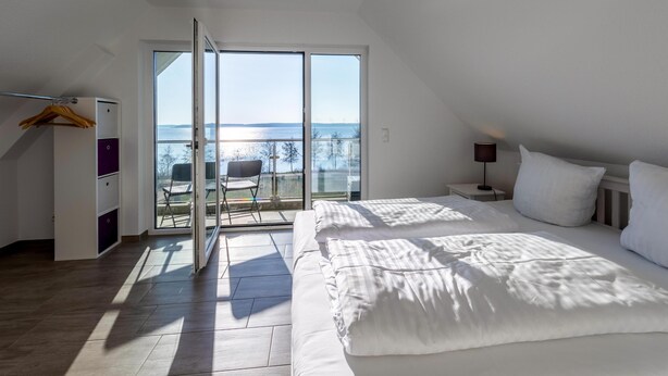 A bedroom with a large bed, a wardrobe, and a sliding glass door leading to a balcony with a view of the sea. - "SchönSicht" Vacation Home in Alt Schwerin, Right on the Lake (Alt Schwerin)