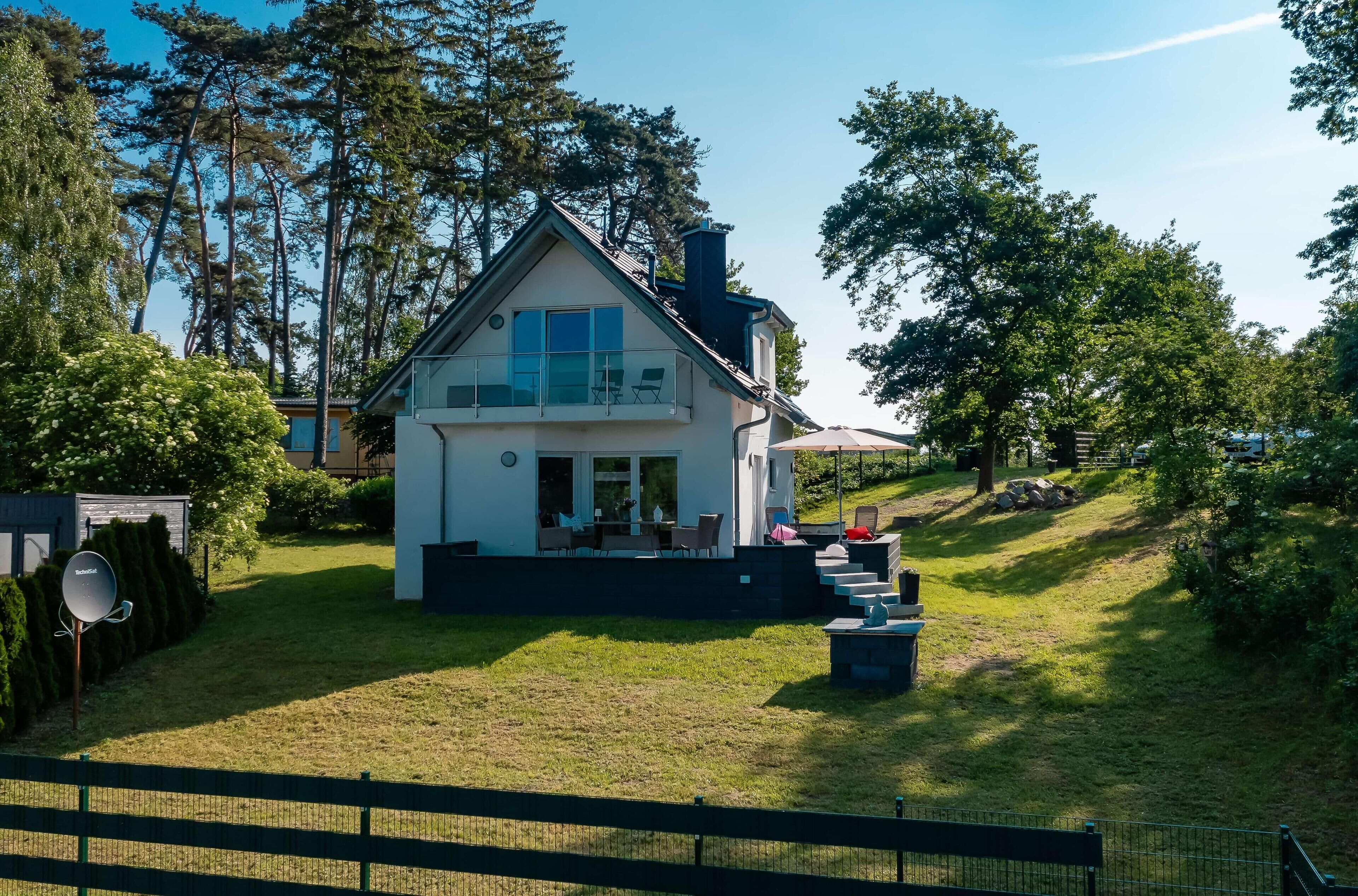 A modern house with a large balcony, surrounded by lush greenery and a well-maintained lawn.