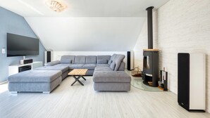 Ein modernes Wohnzimmer mit einem Ecksofa, einem Flachbildfernseher und einem Kaminofen.