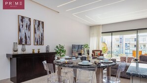 Un soggiorno moderno con un tavolo da pranzo rotondo, sedie trasparenti, un armadio in legno scuro e due quadri astratti alle pareti.