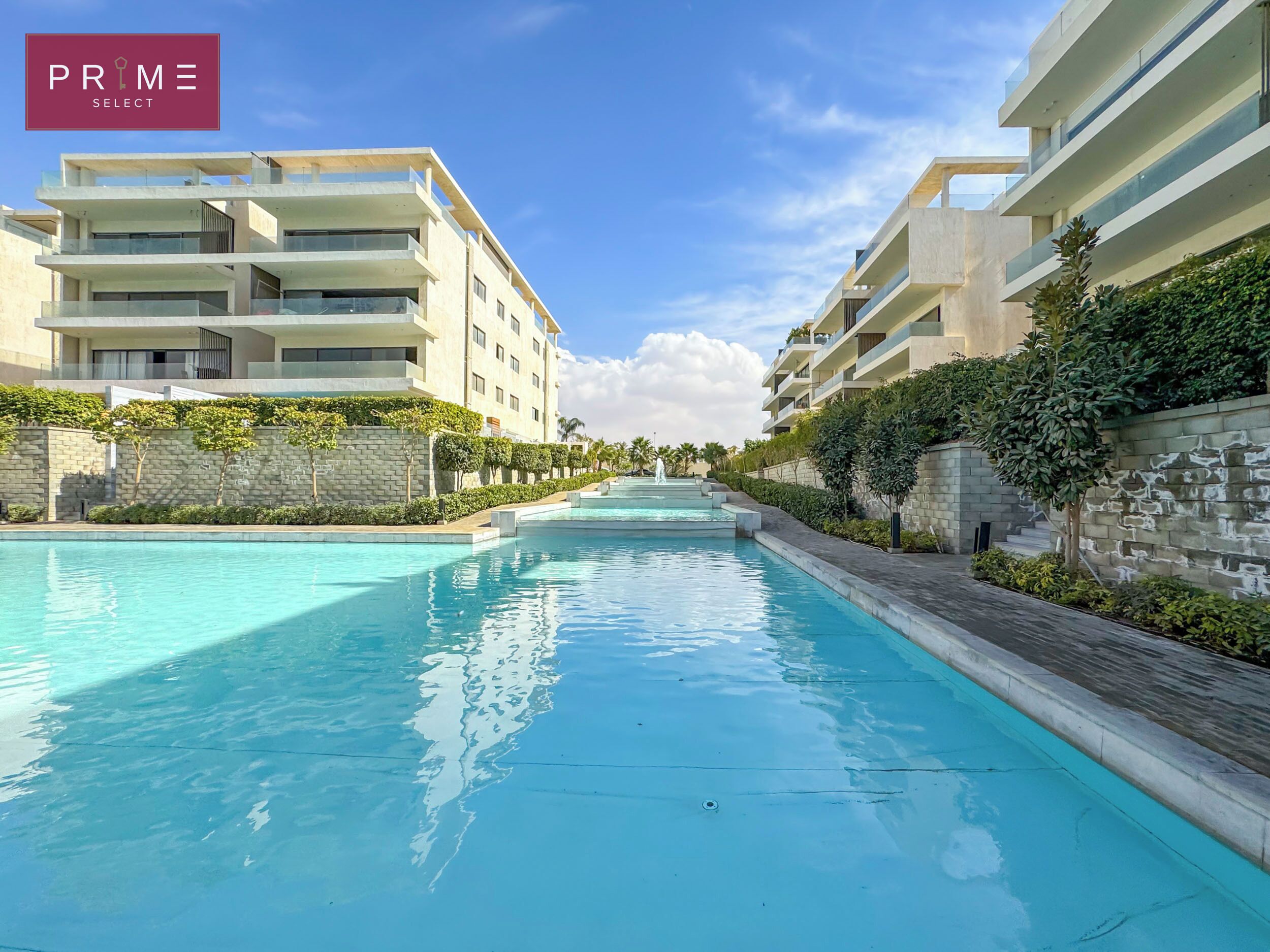 A modern hotel with a central swimming pool, multiple balconies, and lush greenery.