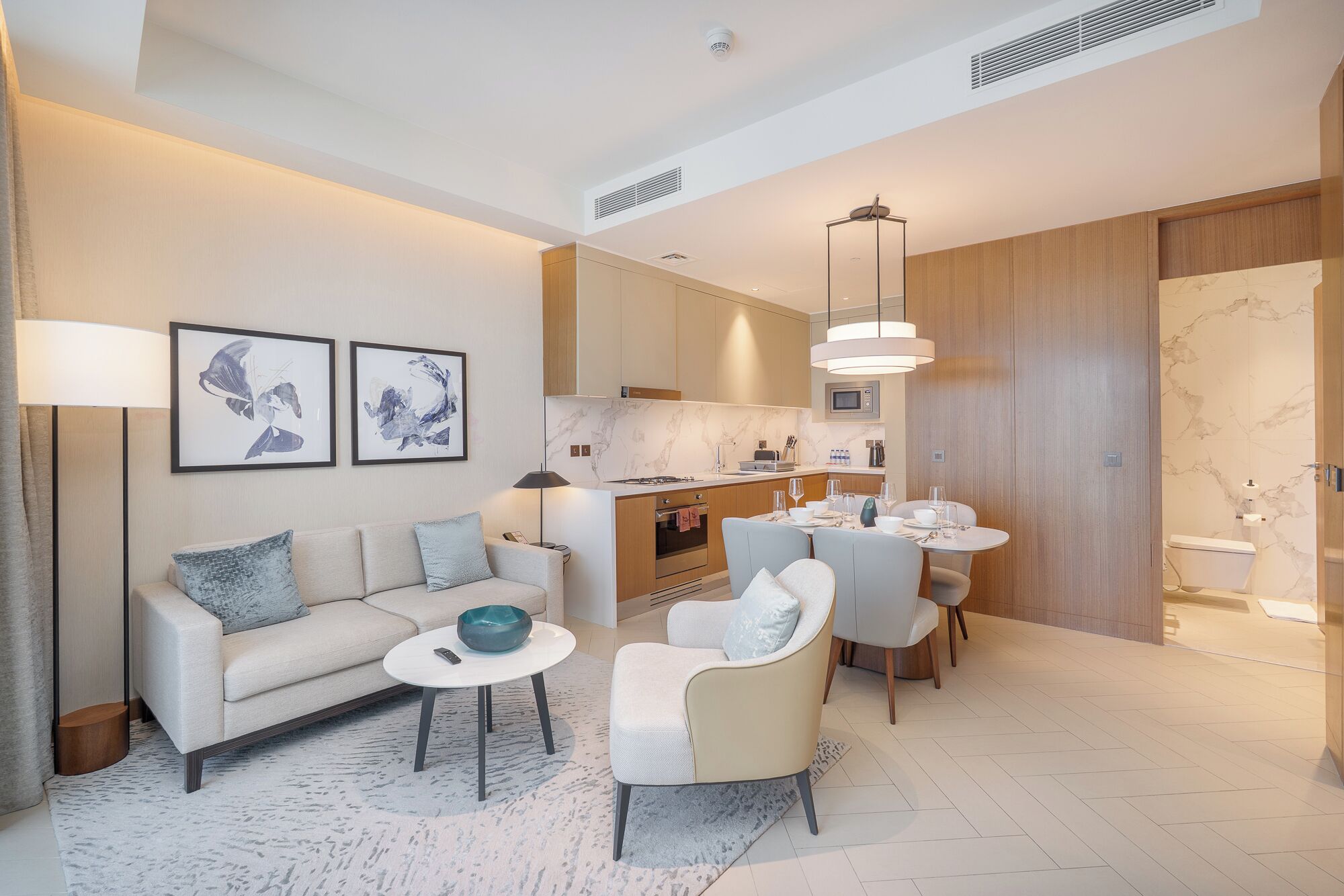 Une chambre d’hôtel moderne équipée d’un canapé, de fauteuils, d’une table à manger et d’un coin cuisine.