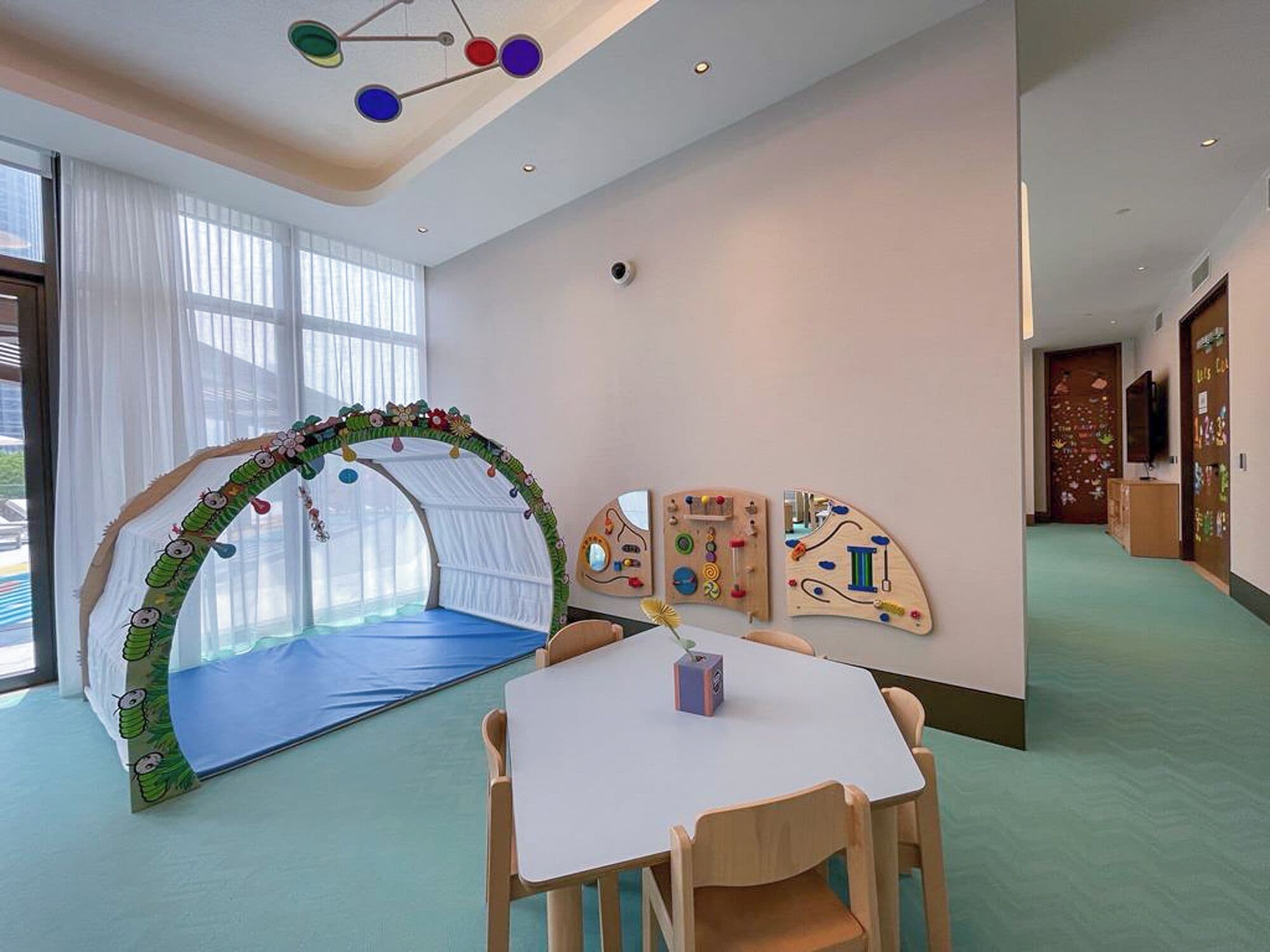 Un'area giochi per bambini con una struttura da arrampicata, un tavolo con sedie e giochi didattici appesi al muro.