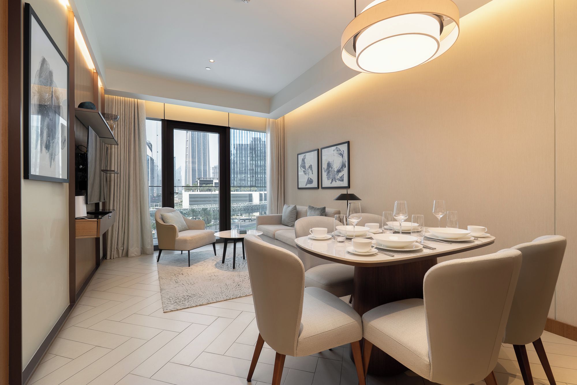 A modern hotel room with a dining area, large windows, and artwork on the walls.