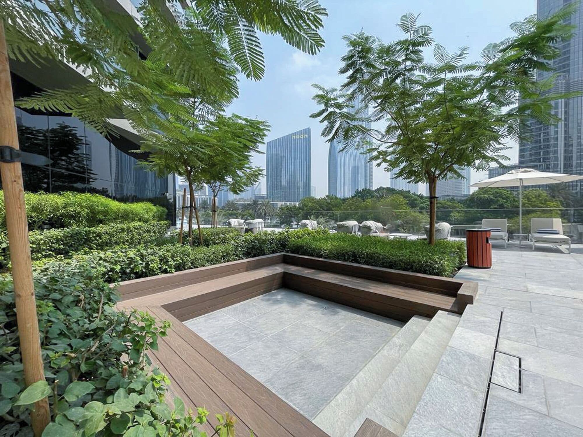 A rooftop garden with a seating area, surrounded by greenery and modern buildings in the background.
