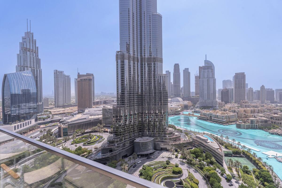 Un immeuble de grande hauteur doté d’une façade incurvée en verre, entouré d’autres gratte-ciel et bordé d’une zone riveraine avec une piscine.