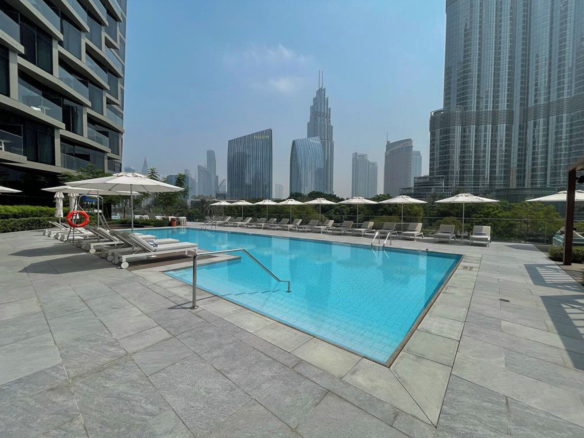 A swimming pool with lounge chairs and umbrellas, surrounded by high-rise buildings.
