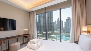 Ein Hotelzimmer mit einem großen Bett, einem Schreibtisch, einem Fernseher und einem Balkon mit Blick auf die Stadt.