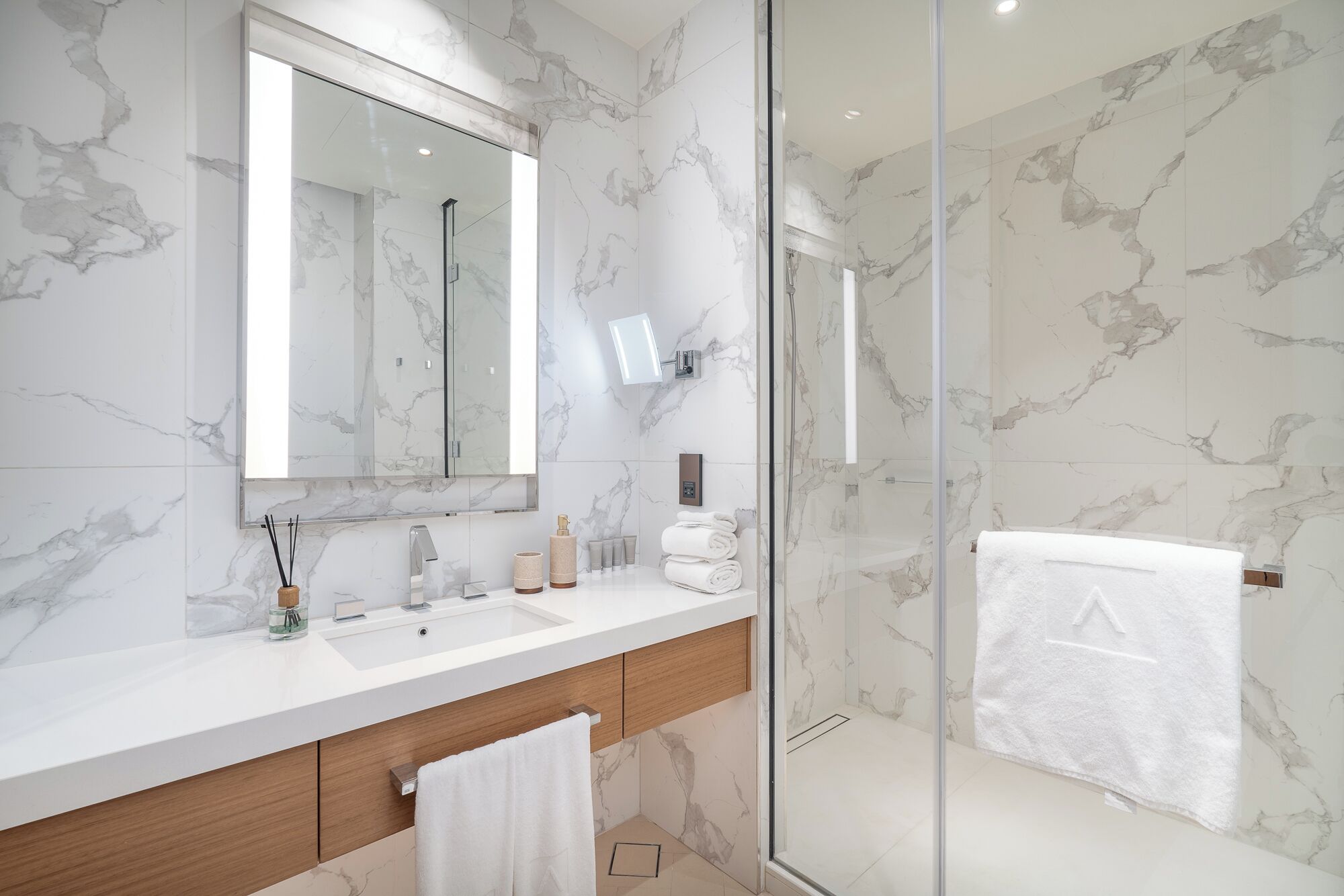 Une salle de bain moderne avec un pare-baignoire en marbre, un grand miroir, une douche en verre et un meuble-lavabo en bois.