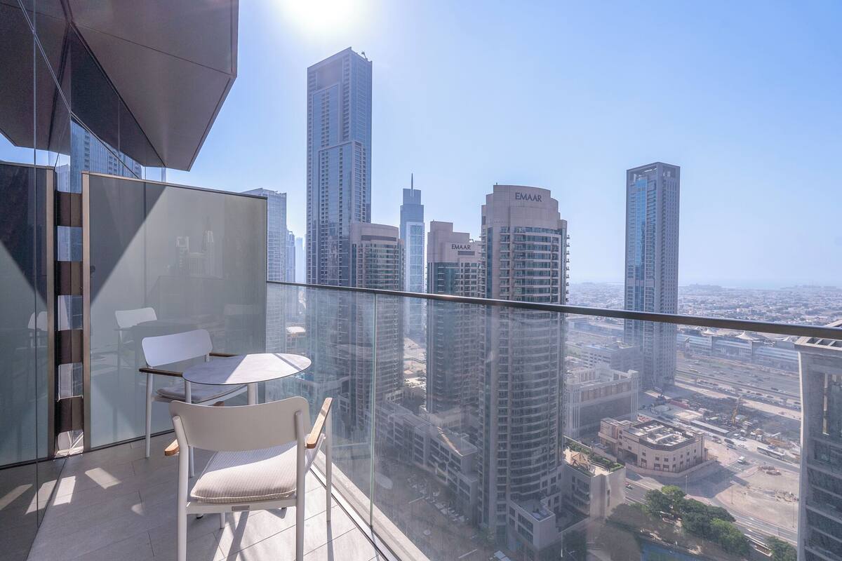 Un balcon avec une paroi en verre, une chaise blanche et une table.