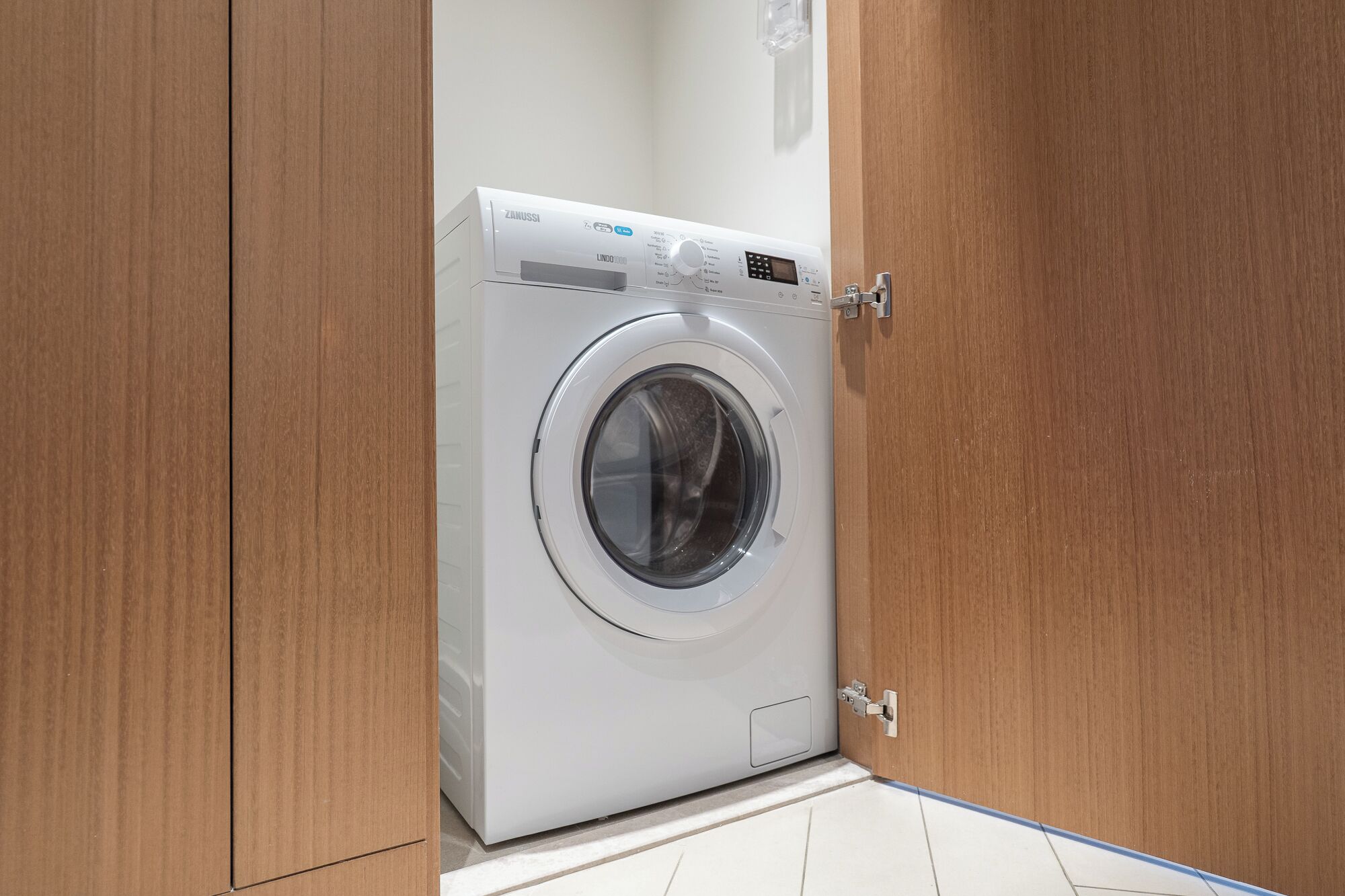 A front-loading washing machine in a wooden cabinet.