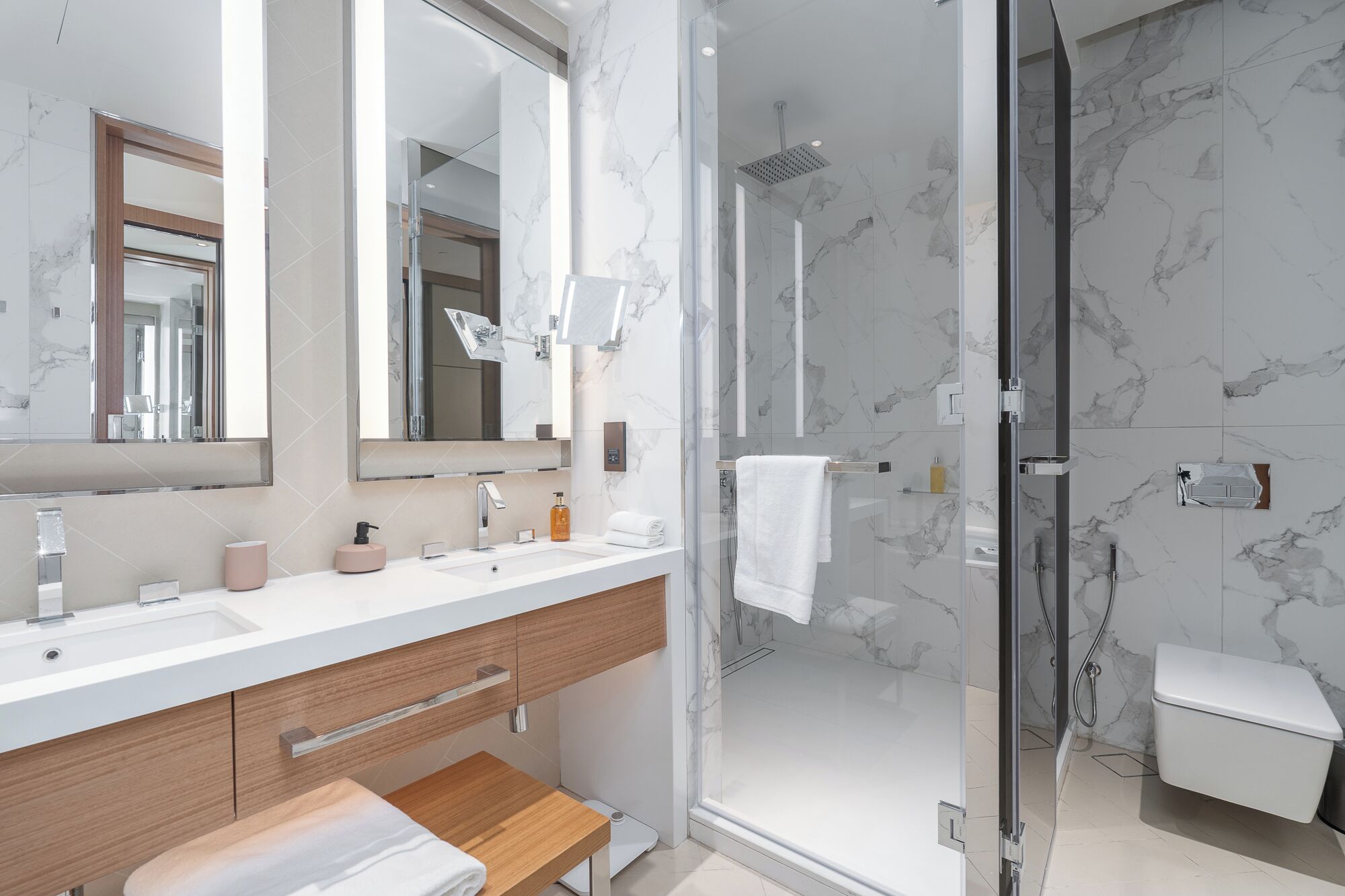 Un baño moderno con salpicadero de mármol, ducha con mampara de vidrio, tocador con lavabo y un espejo.