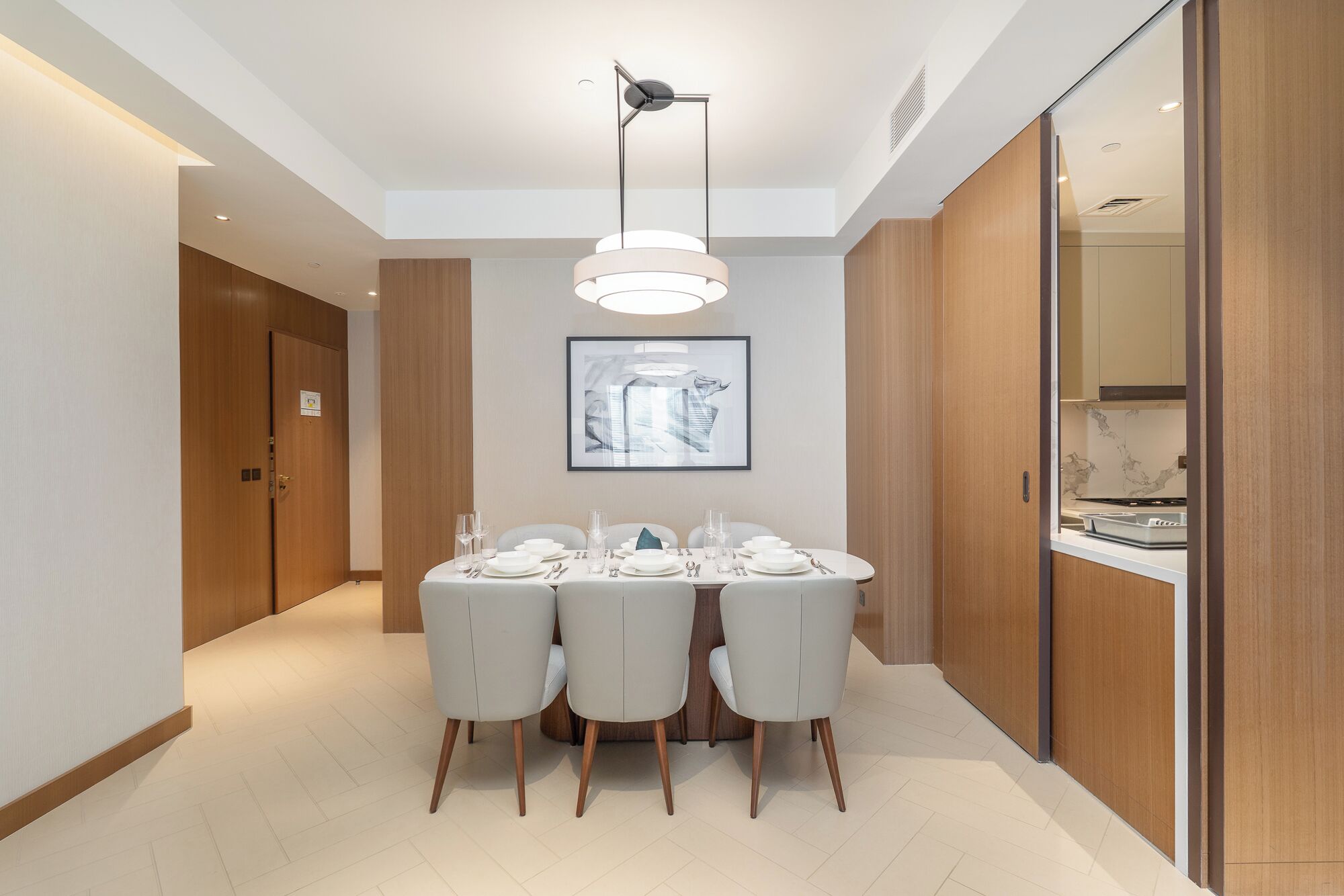A modern dining area with a round table set for four, a pendant light, and a framed artwork on the wall.