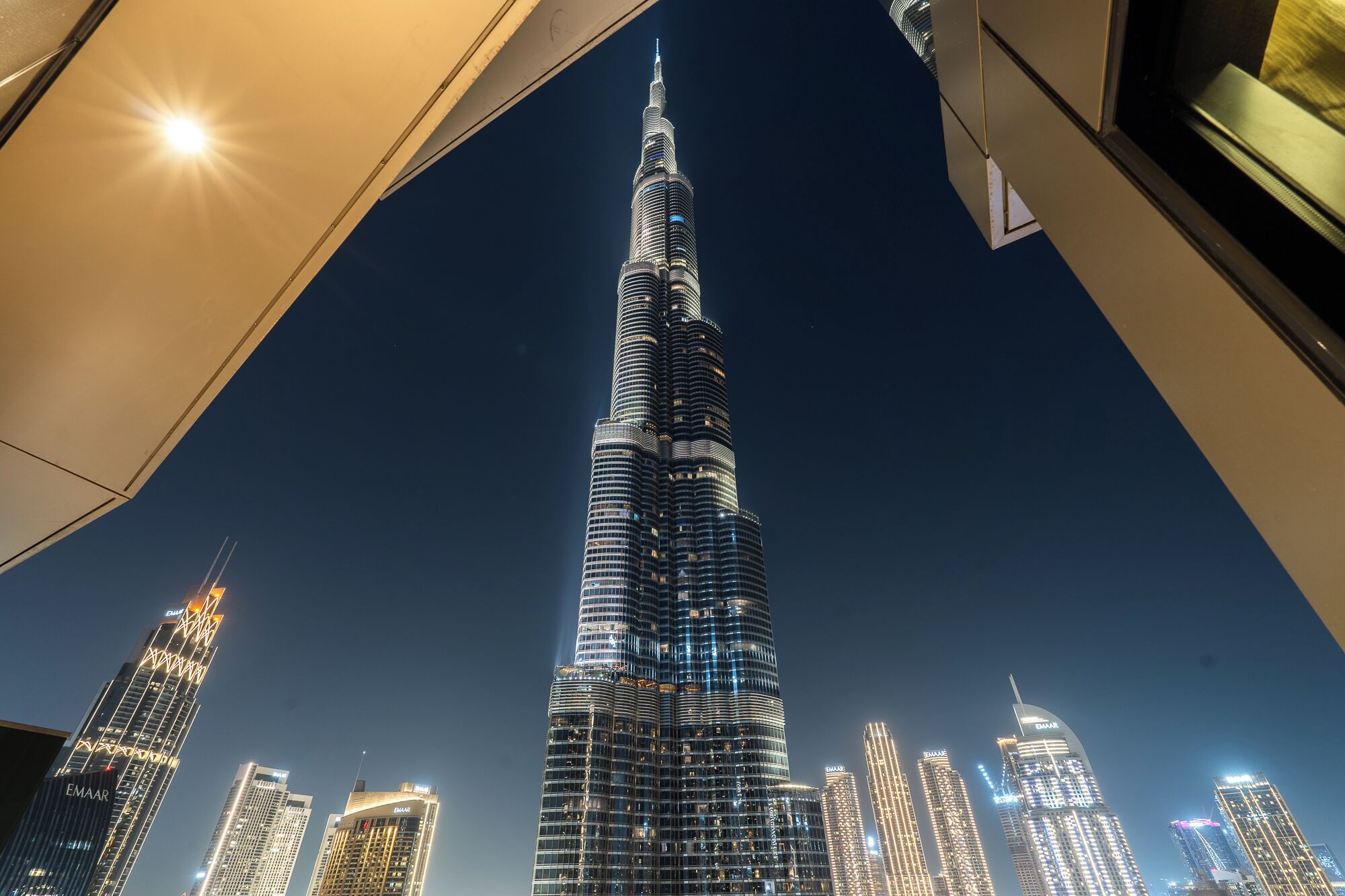 A nighttime view of the Burj Khalifa, surrounded by other illuminated skyscrapers.