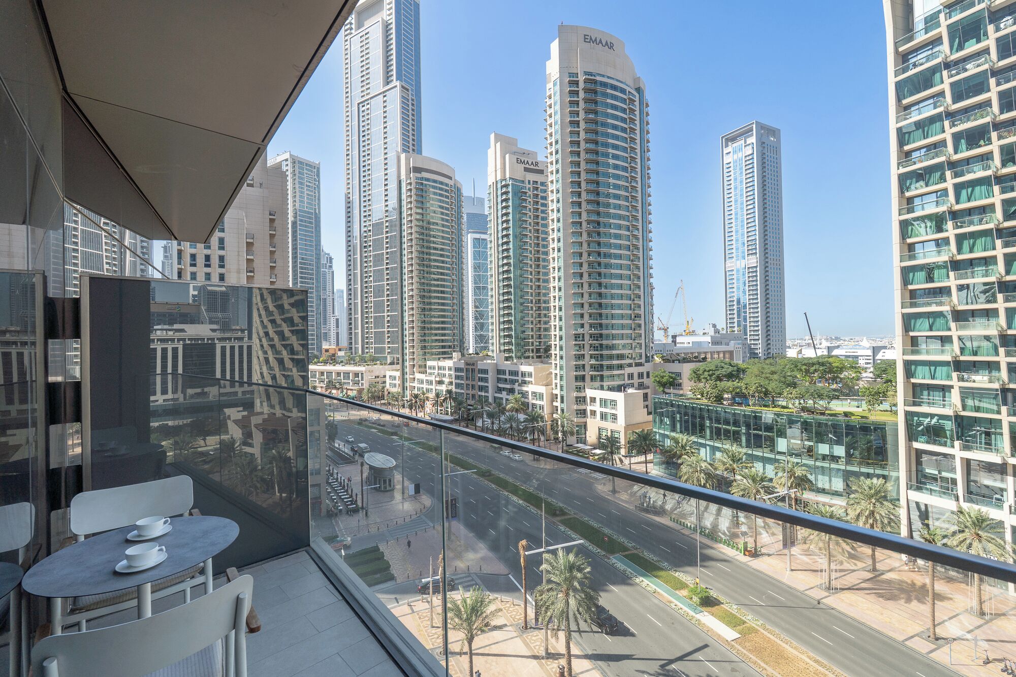 Moderni hotellihuone, jossa on parveke, jolta avautuu näkymä kaupungin siluettiin ja korkeisiin rakennuksiin.