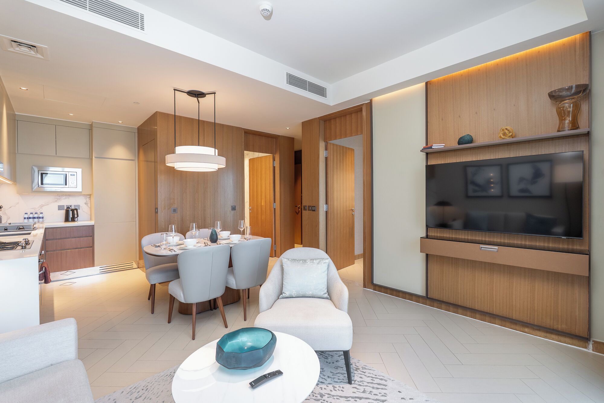 A modern living room with a dining area, a flat-screen TV, and a kitchen with a microwave.