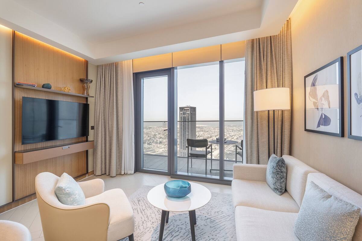 Une chambre d’hôtel moderne dotée d’une grande télévision, de sièges confortables, d’un balcon offrant une vue sur la ville et d’une grande fenêtre.