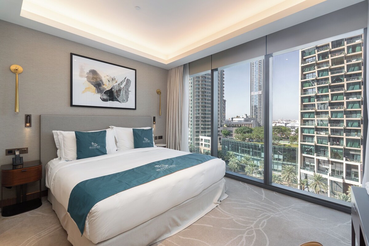 Habitación de hotel moderna con una cama grande, una mesita de noche, un cuadro enmarcado y vistas a edificios altos.