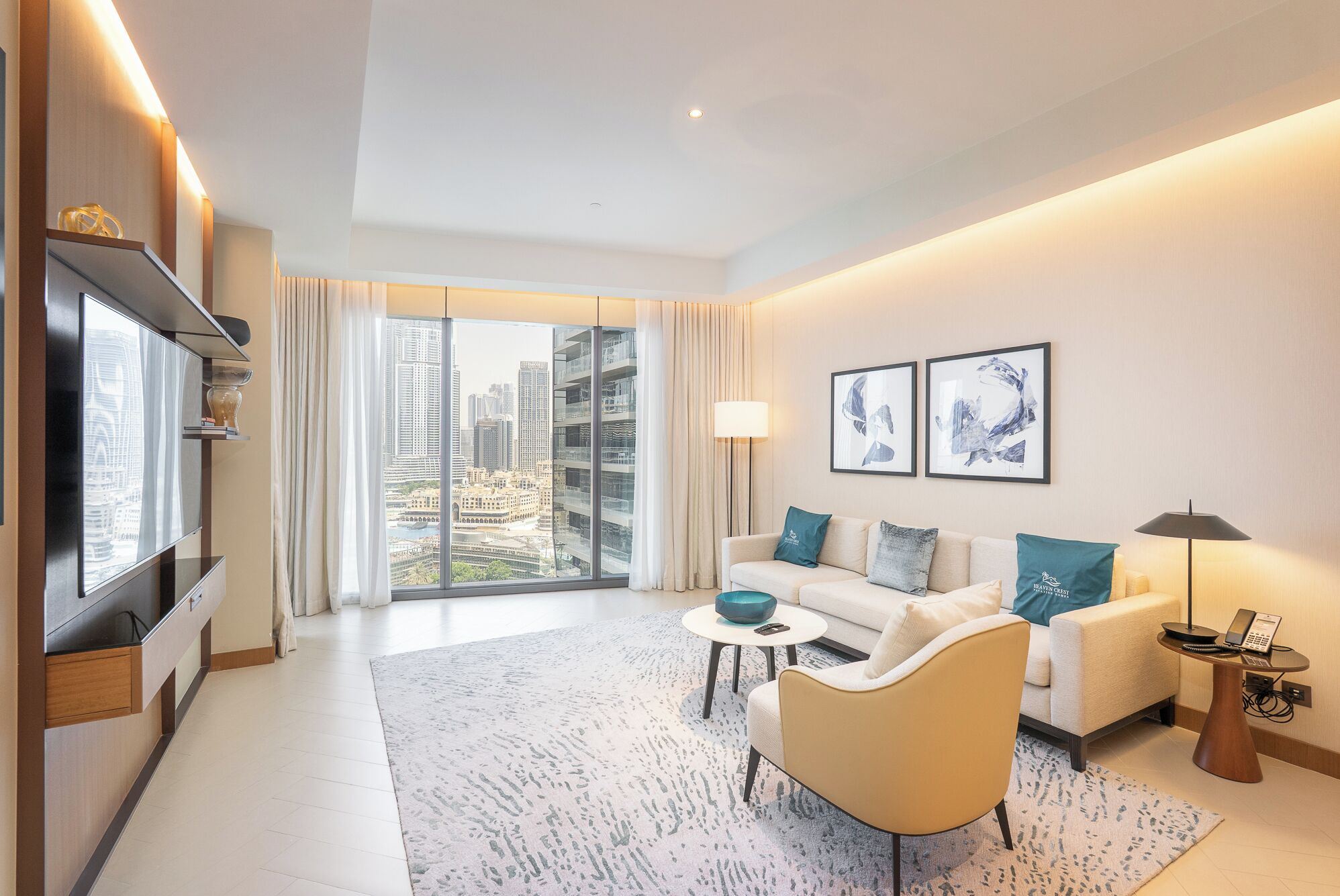 A modern hotel room with a large window offering a city view, a sofa set, a coffee table, a TV, and a lamp.