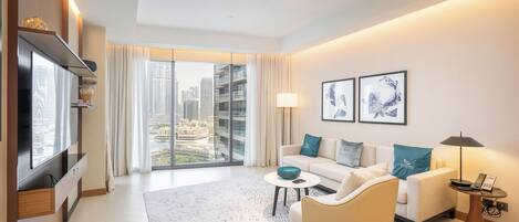 A modern hotel room with a large window offering a city view, a sofa set, a coffee table, a TV, and a lamp.