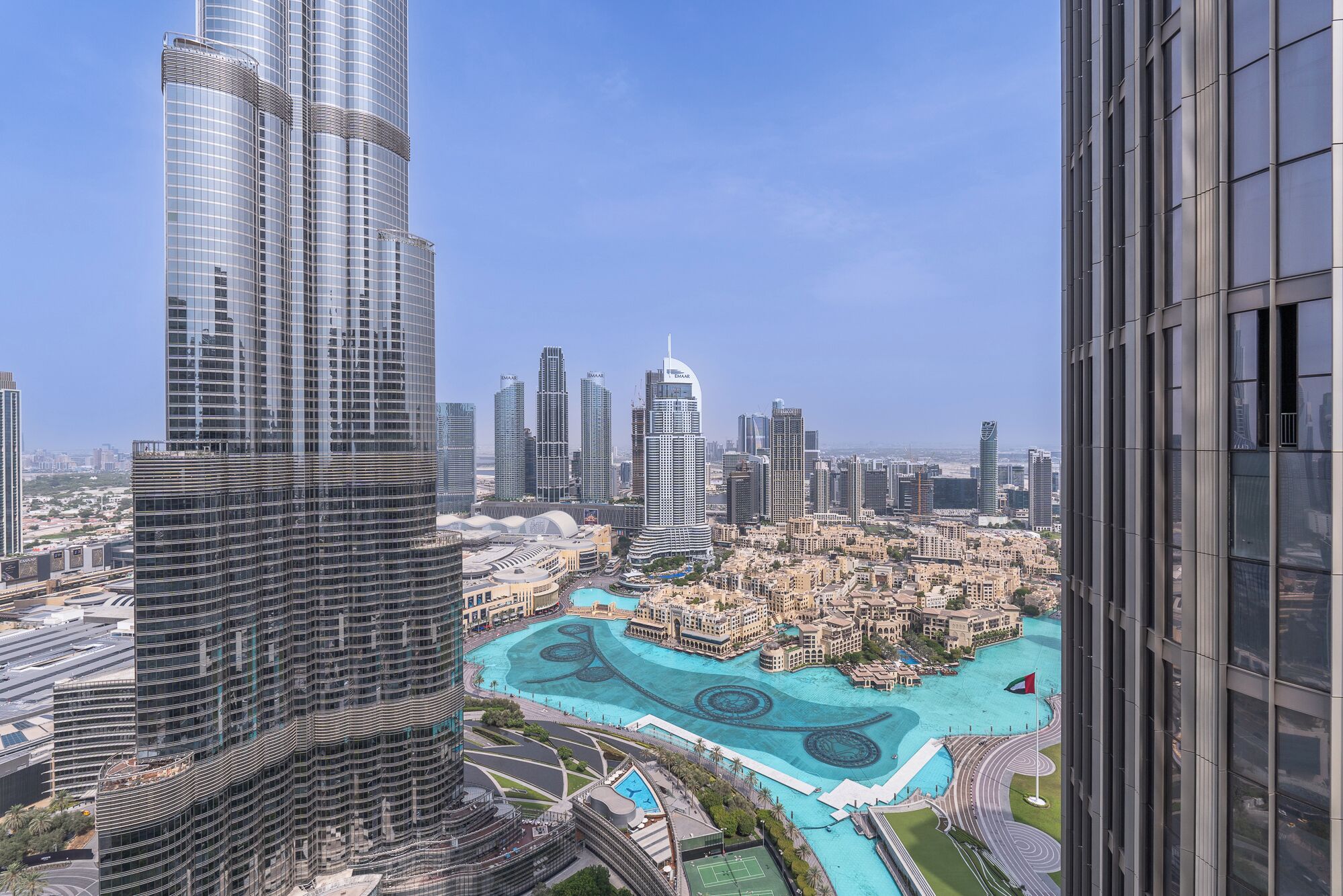 A high-rise building with a modern glass facade, surrounded by other tall buildings and a large, landscaped area with a pool.
