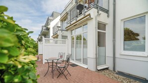 A patio with a table and chairs, a white fence, and a building with balconies and large windows. - Vacation apartment "Abendsonne" with a view of the Müritz (Waren (Müritz))