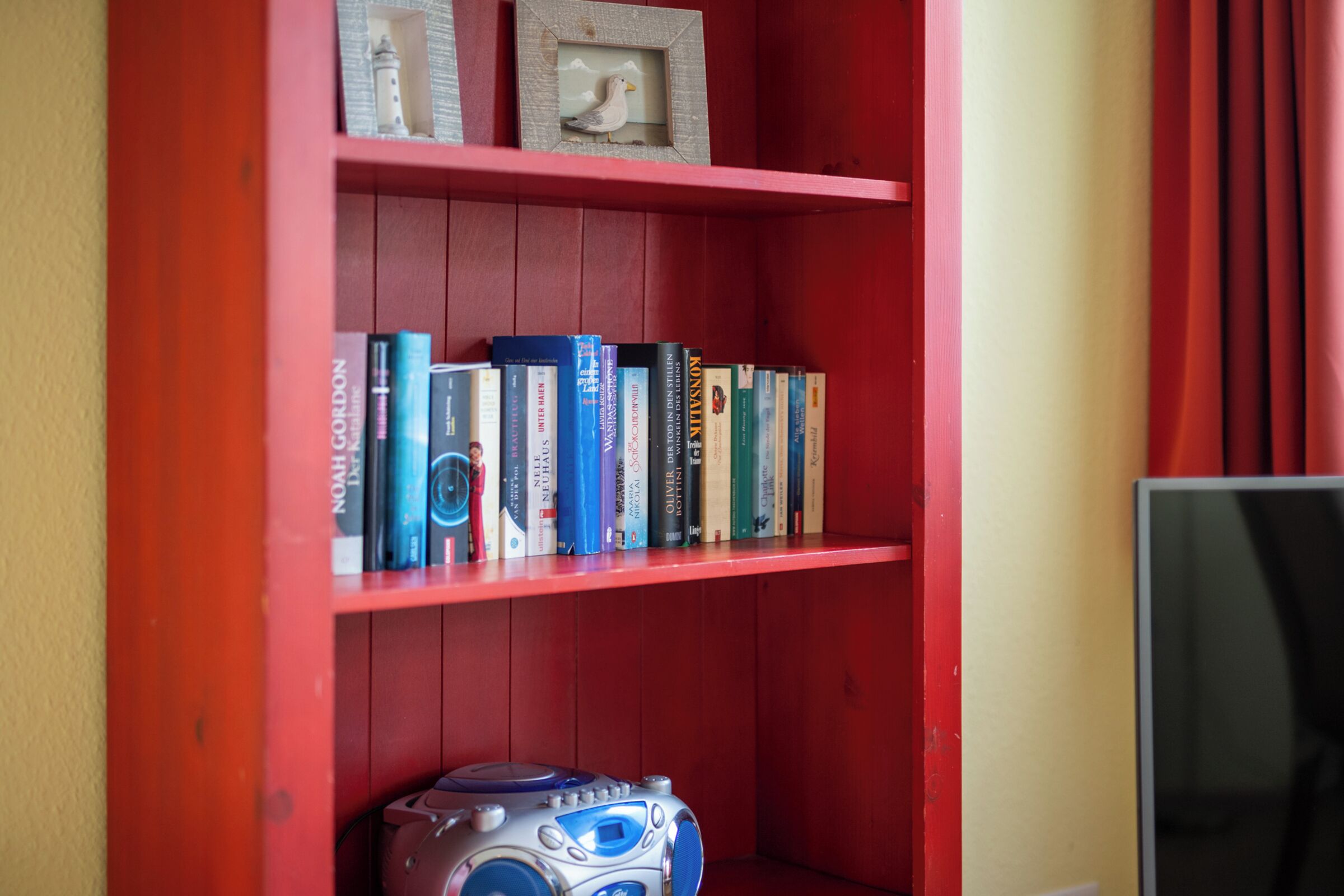 Una estantería roja con varios libros y una pequeña figurita.