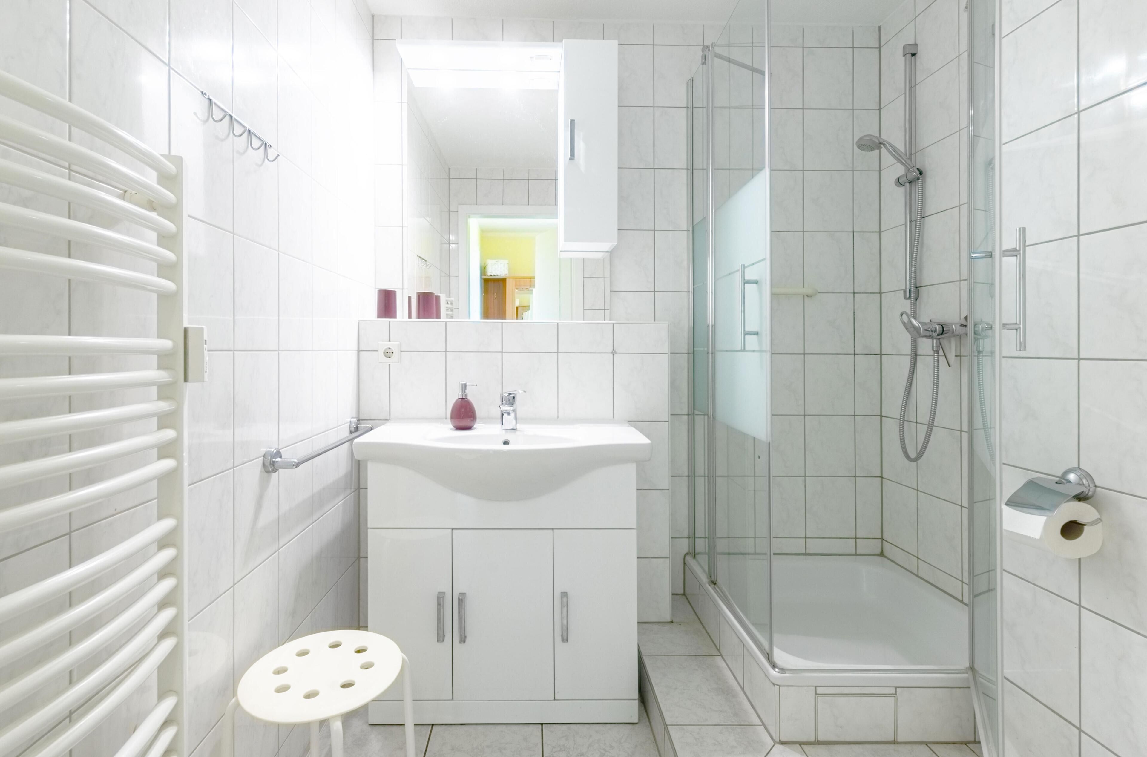Ein modernes Badezimmer mit einem weißen Waschbecken, einer Duschkabine aus Glas und einem weißen Heizkörper.