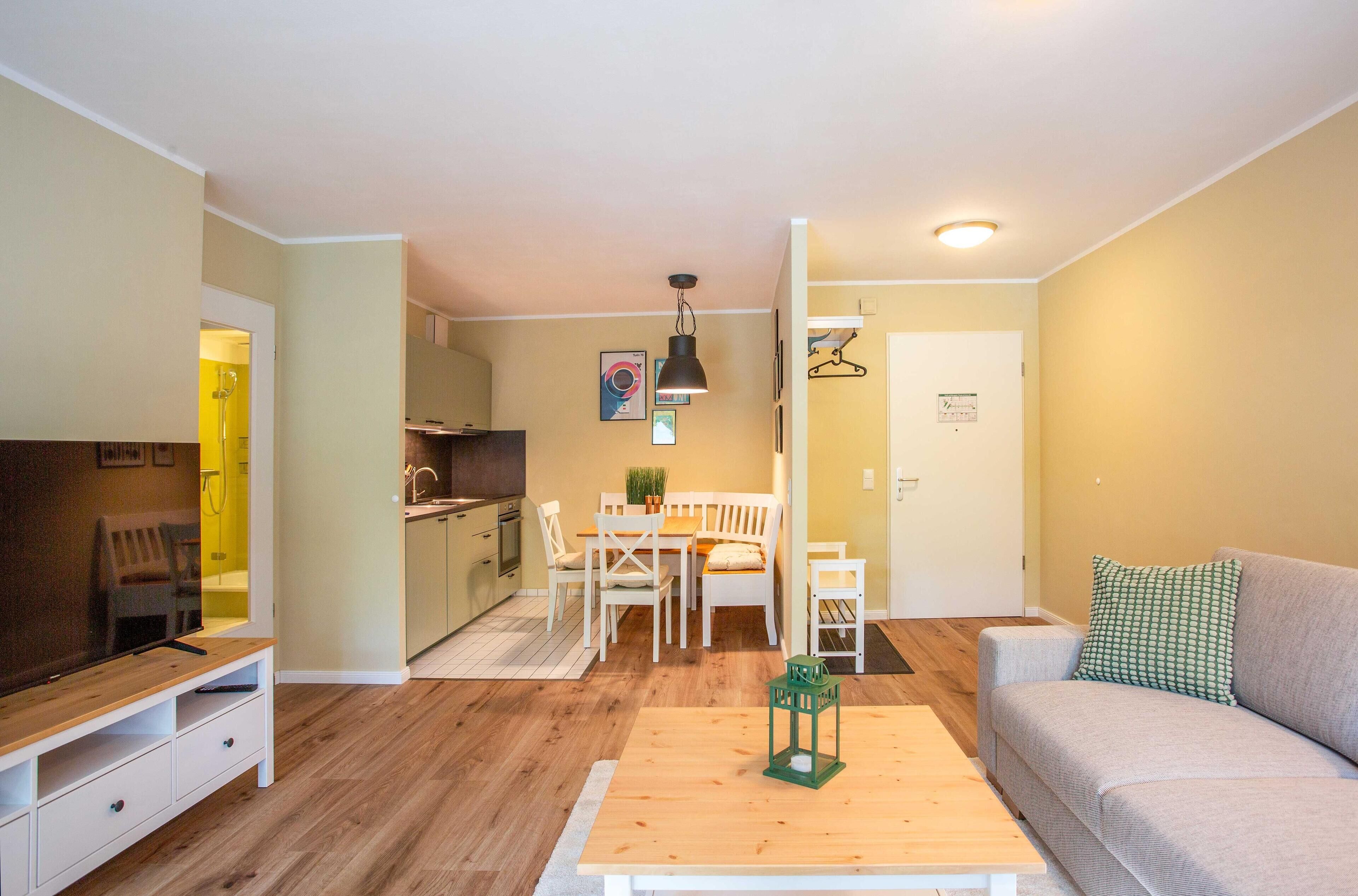 Een moderne woonkamer met een houten salontafel, een grijze bank en een eethoek met een witte tafel en stoelen.