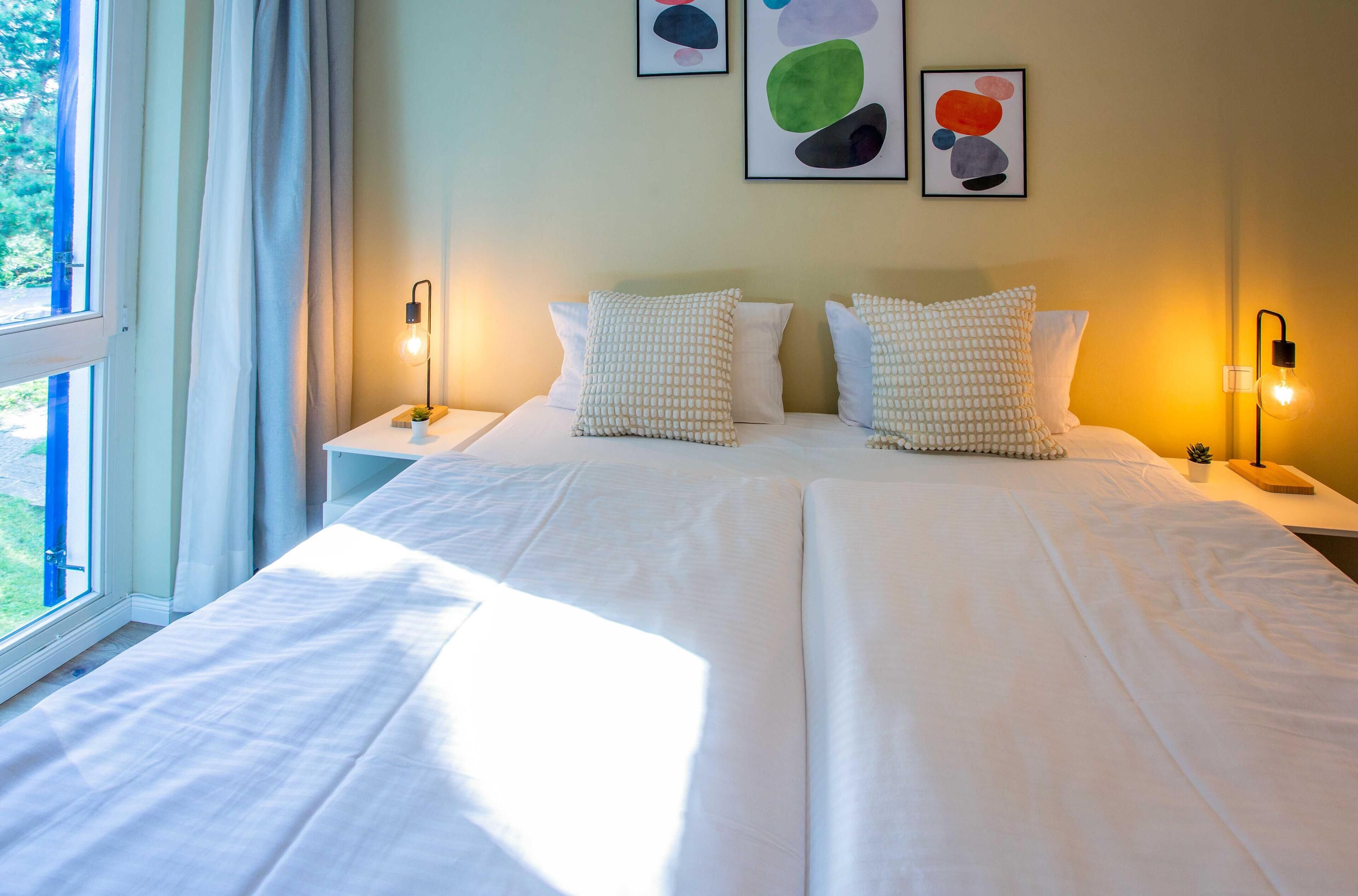 A double bed with white linens, two bedside tables with lamps, and abstract wall art.