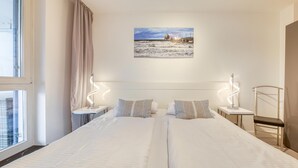 Habitación de hotel con dos camas, vista a la playa y al paisaje urbano a través de la ventana.